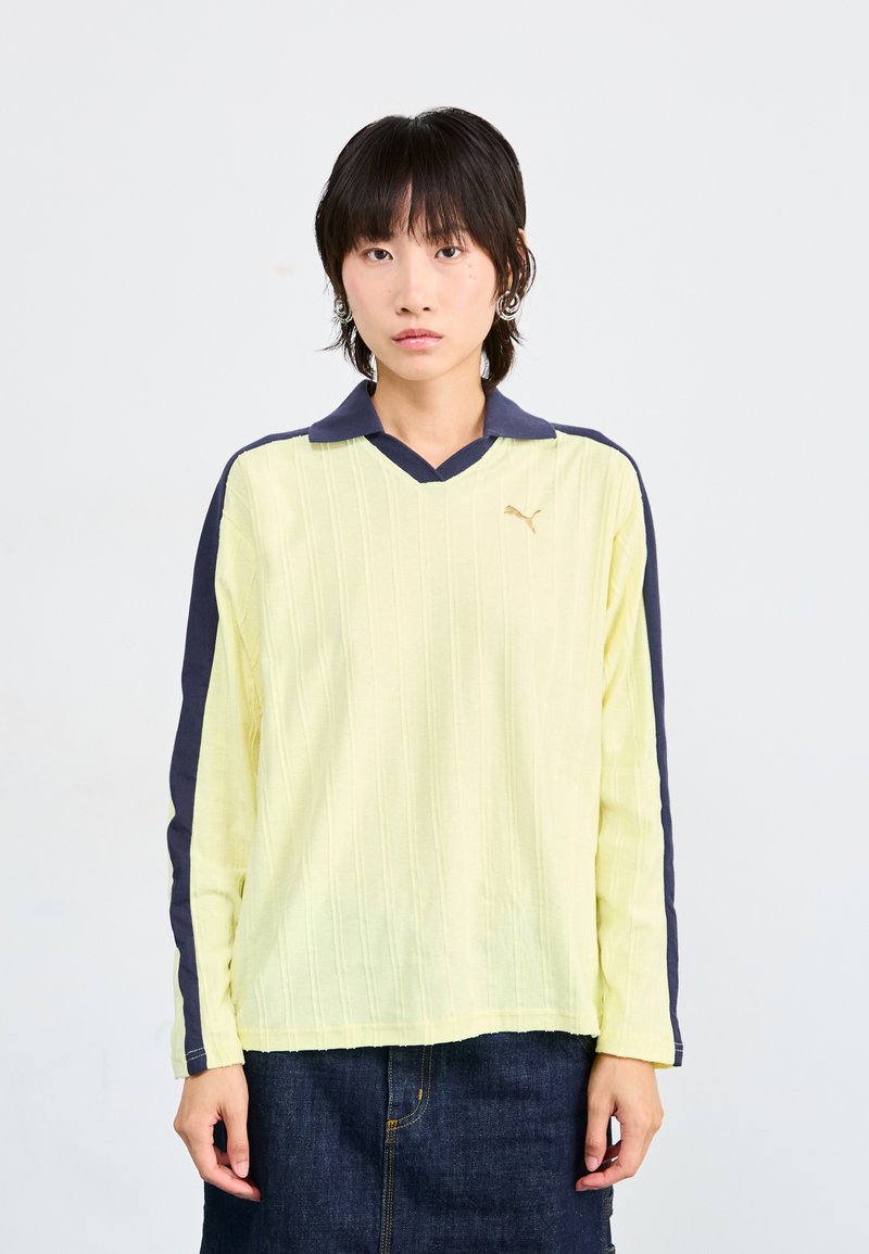 Chemise jaune à manches longues avec un motif à côtes verticales, col et manches bleu marine, dotée d'un petit logo doré sur la poitrine.