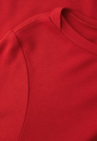 Roter Baumwollstoff mit einer glatten Textur, ausgestattet mit einem runden Halsausschnitt und einer leichten Nahtdetail an der Schulter.