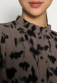 Brown and black patterned shirt with ribbed texture, a mandarin collar, and black buttons down the front.