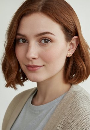 Goldene herzförmige Ohrringe, weiche Textur, getragen mit einem hellgrauen Shirt und einer beigen Strickjacke, dazu ein natürlicher Make-up-Look und ein Bob-Haarschnitt.