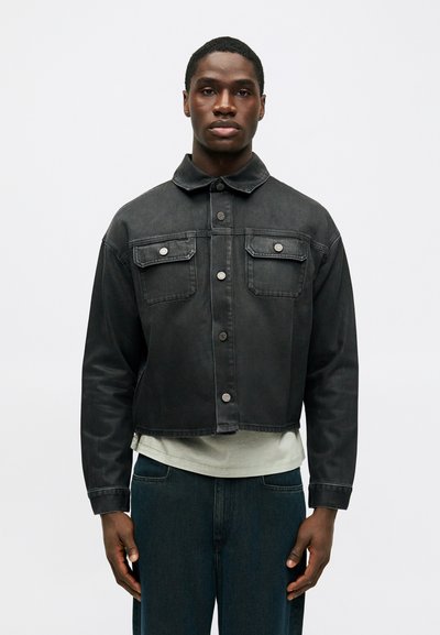 Veste en denim noir au design court, fermeture à boutons sur le devant, deux poches poitrine et col classique. Le tissu a une texture lisse.