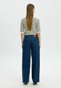 Vida blå denimjeans med vida ben, hög midja, en läderlapp på baksidan och en randig, figurnära topp med tre fjärdedelars ärm.