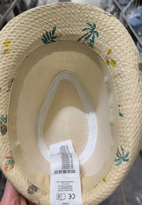 Straw sun hat with palm tree and flower prints, showing inner lining and fabric care label with washing instructions.