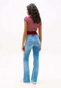 Top de manga corta a rayas rojas y blancas combinado con vaqueros acampanados de color azul claro, mostrando una textura de denim clásica y detalles en los bolsillos traseros.