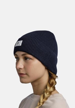 Navy ribbed knit beanie with a flat, rectangular tag featuring branding. Soft texture with a snug fit, suitable for colder weather.