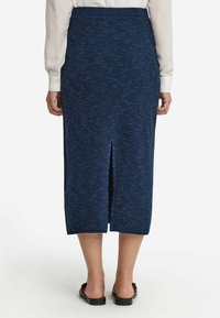 Stickad marinblå midiklänning med strukturerad yta, bakslits och midjeband. Kombinerad med en vit knapp-up skjorta och svarta sandaler.