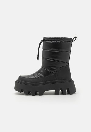 Zwarte gewatteerde enkellaarsjes met een quiltstructuur, stevige chunky rubberen zool, verstelbaar trekkoord aan de bovenkant en een gedefinieerd grippatroon.