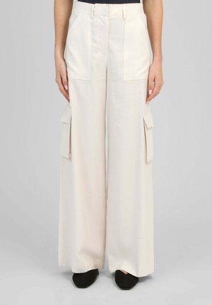 Pantalon écru à jambes larges avec poches plaquées devant et poches cargo latérales, porté avec des chaussures à pointe noires.