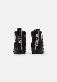 Stivaletti neri da caviglia con una texture trapuntata, dotati di accenti bianchi con il logo "JOTT" e "PALLADIUM" sul retro e una suola in gomma resistente.