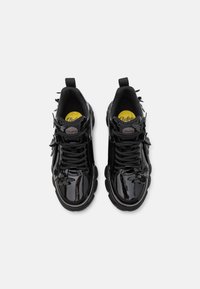 Black patent leather sneakers with chunky soles, floral accents on the sides, and black laces. Features cushioned insoles and looped heel tabs.