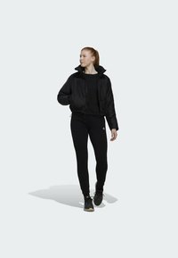 Zwarte cropped pufferjack met een hoge kraag, gecombineerd met een zwarte lange mouwen top en zwarte leggings. Zwarte sportschoenen maken de outfit compleet.