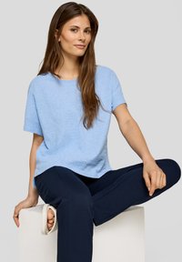 Himmelblaues, strukturiertes Kurzarmtop kombiniert mit dunkelblauen Hosen. Das Outfit zeichnet sich durch eine lockere Passform und ein einfaches, klares Design aus.