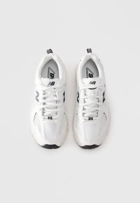 Une paire de chaussures de course New Balance blanches avec un logo noir et des lacets blancs, vue de dessus sur un fond blanc.