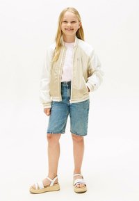 Chaqueta bomber beige y blanca, camiseta rosa, pantalones cortos de mezclilla y sandalias blancas con suelas de plataforma. Tela suave y diseño casual.