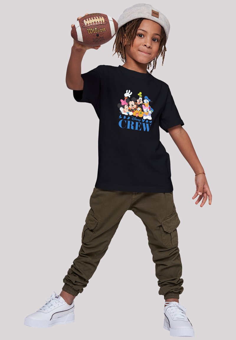 Camiseta negra de manga corta con personajes de Disney en multicolor y el texto "CREW". Combinada con pantalones cargo color oliva y zapatillas blancas.