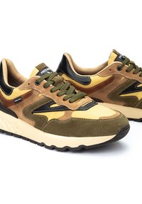 Zapatillas deportivas en marrón y amarillo con materiales de ante y cuero, acentos texturizados, cordones verdes a juego y ribete negro en el talón.