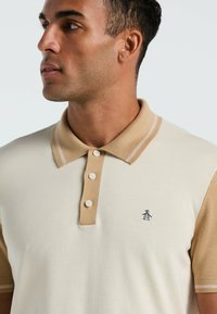 Beige und cremefarbener Poloshirt mit kurzen Ärmeln, aus Baumwollmischung, mit einer Drei-Knopf-Leiste, kontrastierendem Kragen und besticktem Logo auf der Brust.