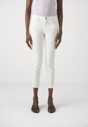 Jeans blancos recortados con un ajuste slim, que cuentan con cinco bolsillos y un cierre de botón. Combinados con sandalias negras de tiras. Textura de tela suave.