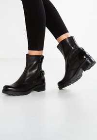 Svarta anklarstövlar av slätt läder, med dragkedja och sidrem, samt klack och mönstrad gummisula.