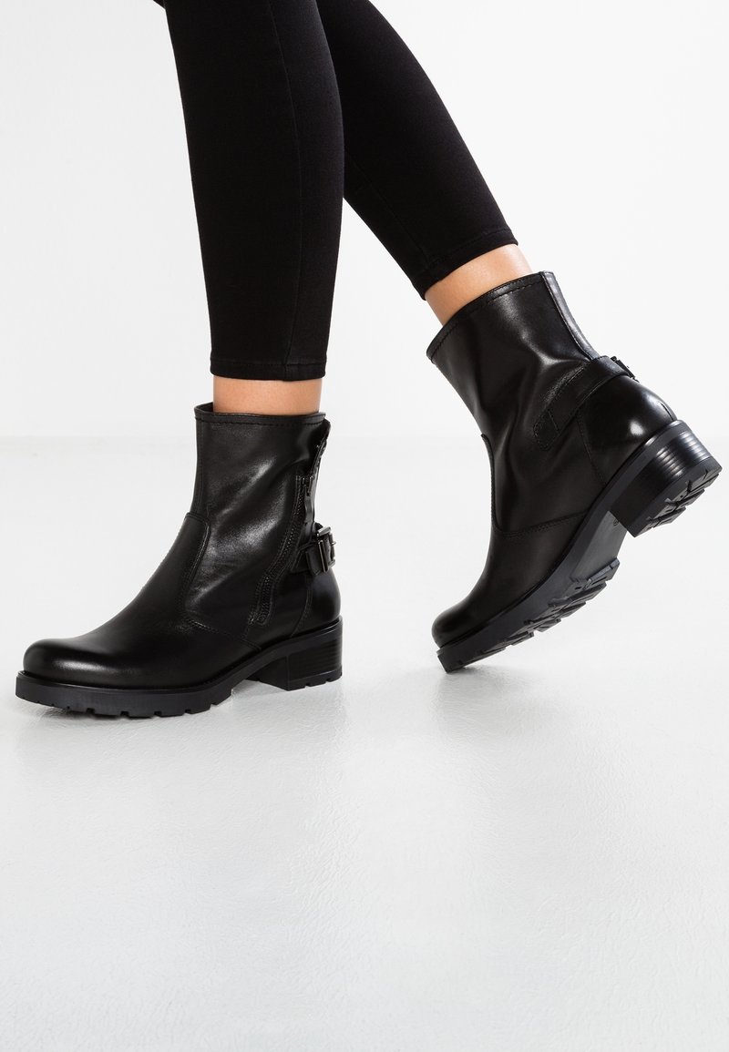 Svarta anklarstövlar av slätt läder, med dragkedja och sidrem, samt klack och mönstrad gummisula.