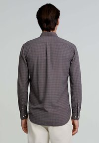 Camisa de manga larga de tela gris con un patrón de cuadros en azul marino y rojo. Presenta un cuello abotonado y puños.