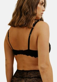 Soutien-gorge en dentelle noire avec des bretelles ajustables, motif floral et fermeture à crochets. La texture semble douce et riche en détails.