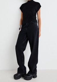 Svart kortärmad topp kombinerad med högmidjade svarta vida jeans. Accessoarer inkluderar vita solglasögon och kraftiga svarta träskor.