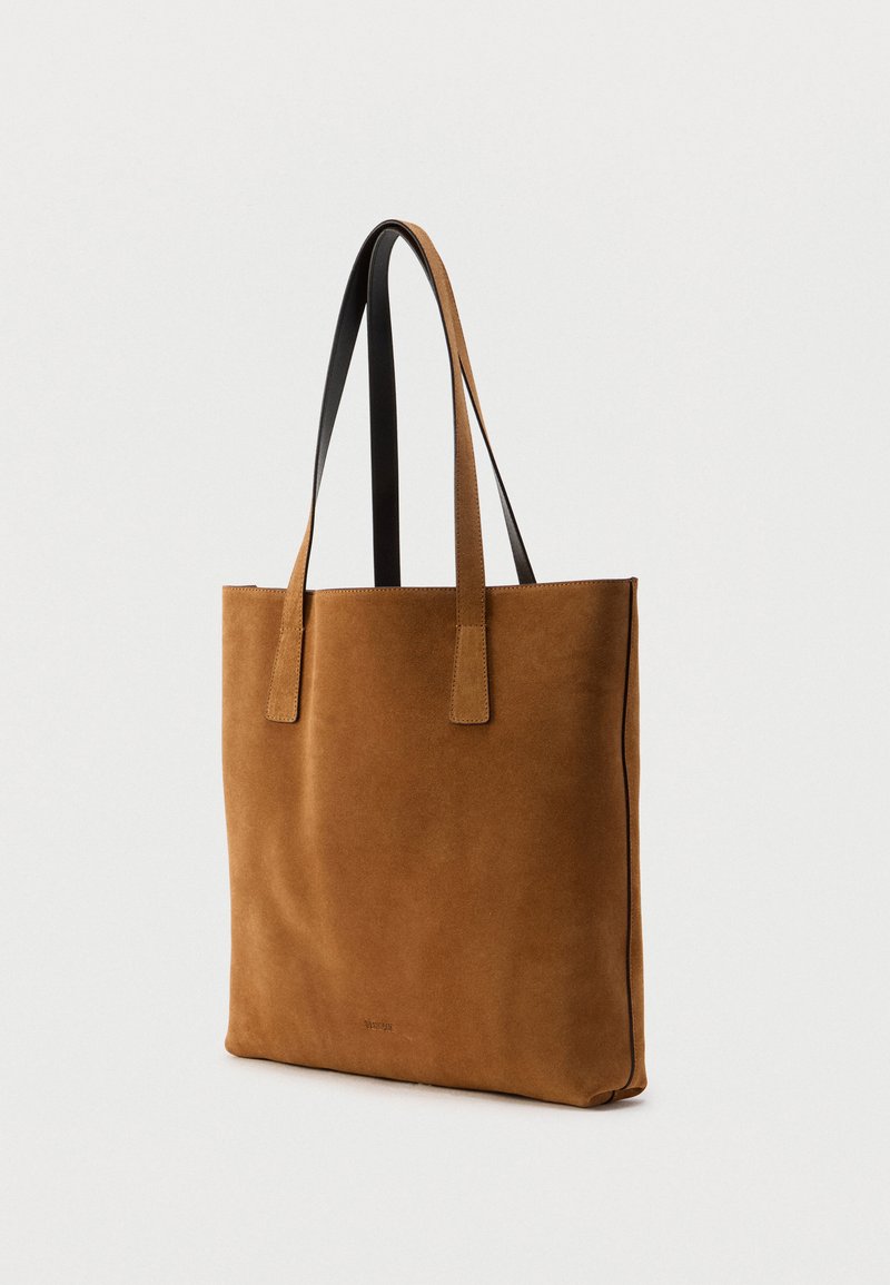 Braune Wildleder-Tasche mit schwarzen Lederhenkeln. Rechteckige Form, glatte Textur, minimalistisch im Design und mit dezentem Markenlogo.