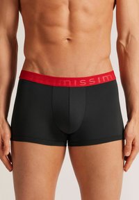Černé boxerky s červeným elastickým pasem, na kterém je logo "Intimissimi". Hladký materiál, přiléhavý střih a přední kapsa.