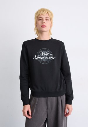 Svart hettegenser laget av bomull med rund hals; har en hvit "Nike Sportswear"-logg i midten og ribbede mansjetter på ermene.
