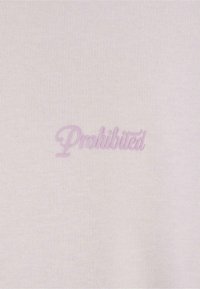 Tissu léger crème avec une texture douce, comportant le mot "Interdit" en cursive rose pâle brodé au centre.