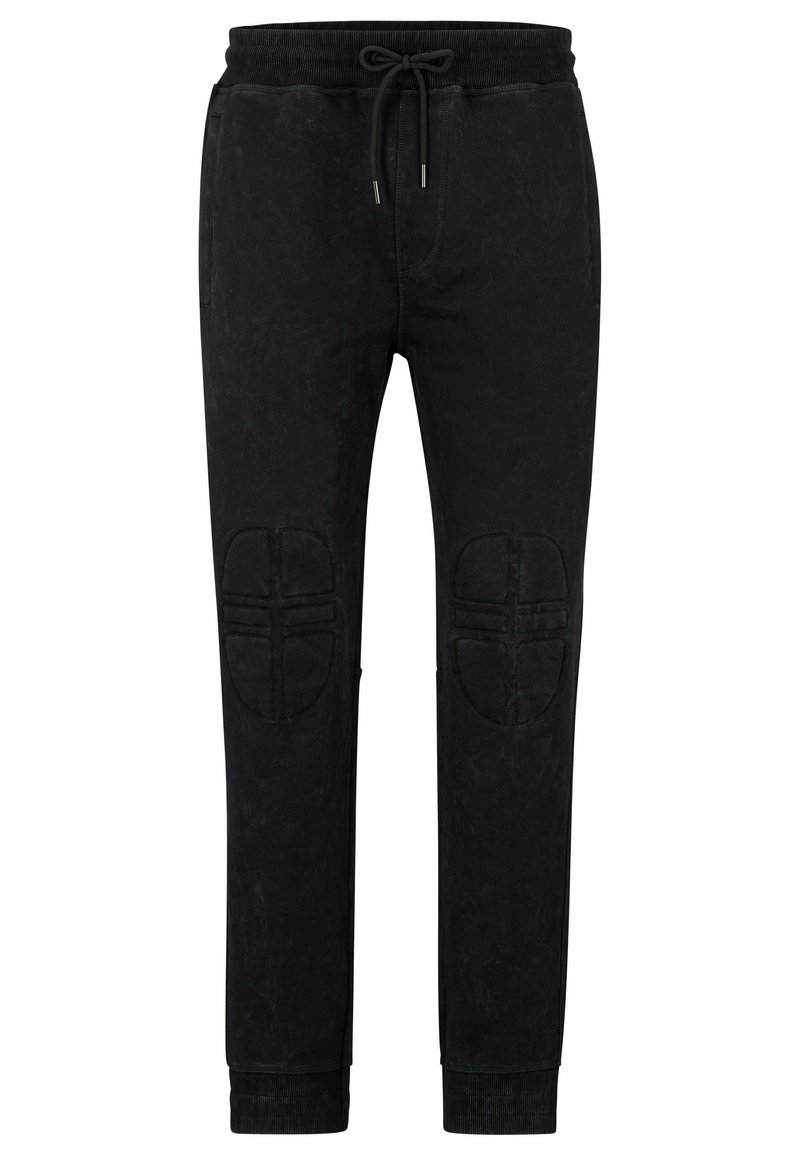 Pantaloni jogger neri in morbido tessuto testurizzato con vita regolabile tramite coulisse e rinforzi sulle ginocchia. Presenta polsini aderenti e tasche laterali.