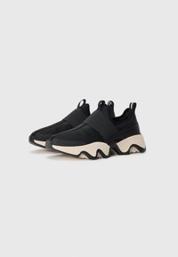 Et par svarte slip-on sneakers med bred elastisk stropp, mesh-overdel, og chunkete beige og svarte bølgete såle på hvit bakgrunn.