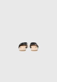 Sandale negre din piele cu un finisaj neted, având un design minimalist al curelei și o talpă din cauciuc bej deschis.