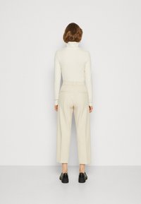 Light-colored turtleneck top paired with high-waisted, wide-leg beige trousers and black platform shoes, seen from the back.
