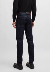 Dark blue denim jeans with a straight-leg cut, featuring a classic five-pocket design, contrast stitching, and a leather patch on the waistband.