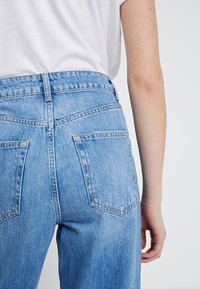 Světle modré džíny s vysokým pasem a volným střihem, vybavené dvěma zadními kapsami a viditelnými švy. Materiál vypadá jako džínovina.