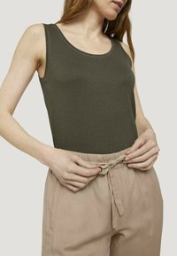 Débardeur vert olive avec un col arrondi, associé à un pantalon beige à cordon de serrage, présentant une coupe décontractée et une texture douce.