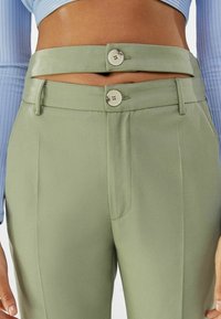 Zielone spodnie z wysokim stanem, z dwoma guzikami z przodu, elegancka tkanina, dopasowany krój oraz kieszenie boczne. Uzupełnione odpinanym paskiem.