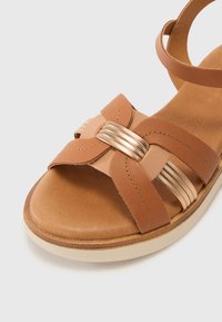 Sandalo in pelle marrone con design a strisce intrecciate, accenti metallici e soletta imbottita. Suola chiara, punta arrotondata.