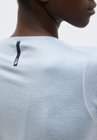 Κοντινό πλάνο του άνω μέρους της πλάτης και του λαιμού ενός ατόμου που φορά ένα ανοιχτό μπλε πουκάμισο με κάθετο μαύρο λογότυπο The North Face κοντά στον γιακά.