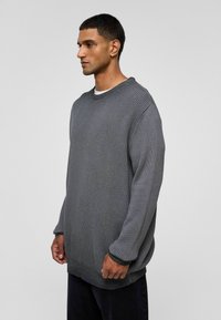 Pull en tricot gris surdimensionné avec une texture côtelée, col rond et manches longues, doté d'une finition contrastante aux poignets et à l'ourlet.