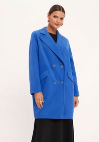 Niebieski płaszcz dwurzędowy z dużymi klapami, dwoma przednimi kieszeniami i guzikami. Gładka tekstura i oversize'owy krój.