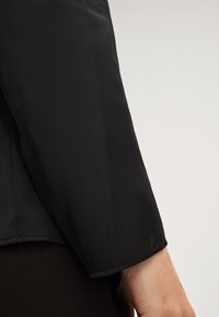 Czarna, długa rękawiczka ma gładką, matową teksturę i czysty brzeg przy nadgarstku, prezentując subtelny, minimalistyczny design.