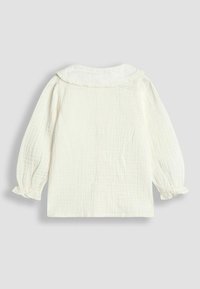 Langärmlige weiße Bluse mit strukturiertem Gewebe, Rüschkragen und elastischen Rüschärmeln, flach auf einem hellgrauen Hintergrund präsentiert.