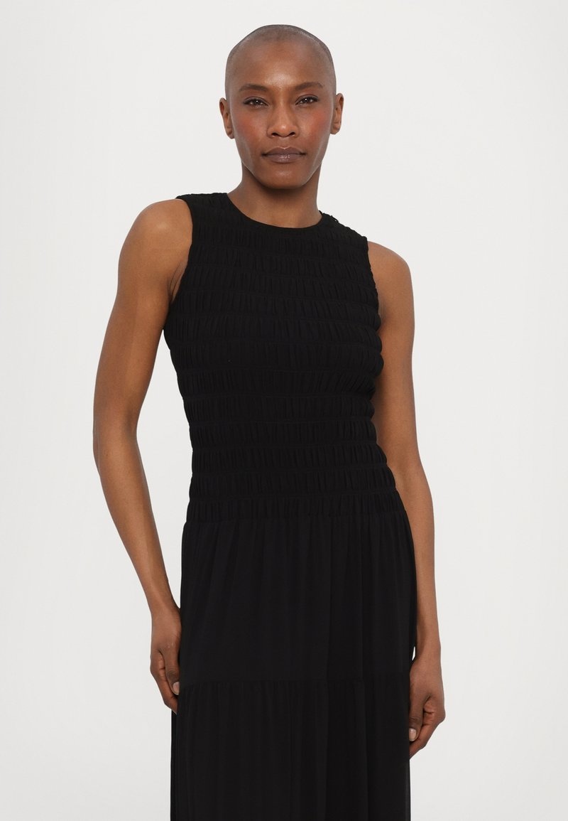 Czarna sukienka bez rękawów z dopasowanym, fakturowanym górnym częściami i zwiewną dolną częścią. Materiał ma subtelne marszczenia i gładkie wykończenie.