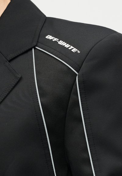 Μαύρο ραμμένο σακάκι στον ώμο με λευκή λεπτομέρεια περιθωρίου και το λογότυπο "OFF-WHITE™" κεντημένο κοντά στον γιακά.