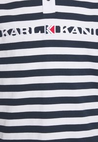 Mörkblå och vit randig polo t-shirt med tvåknapps-öppning; har en broderad logotyp med röda, vita och blå detaljer.