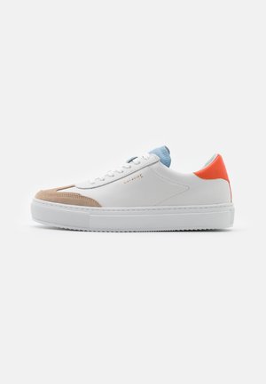 Baskets basses blanches avec bout beige, languette bleu clair, patch orange au talon et semelle blanche sur fond blanc.