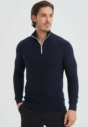Pull à col zippé bleu marine au design ajusté, fabriqué en tissu tricoté avec des manches longues et des poignets et un ourlet côtelés. Détails de fermeture éclair accentués.